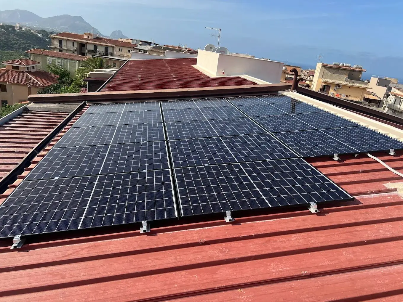 Impianto fotovoltaico installato da Nes su una copertura in lamiera, con case e colline sullo sfondo